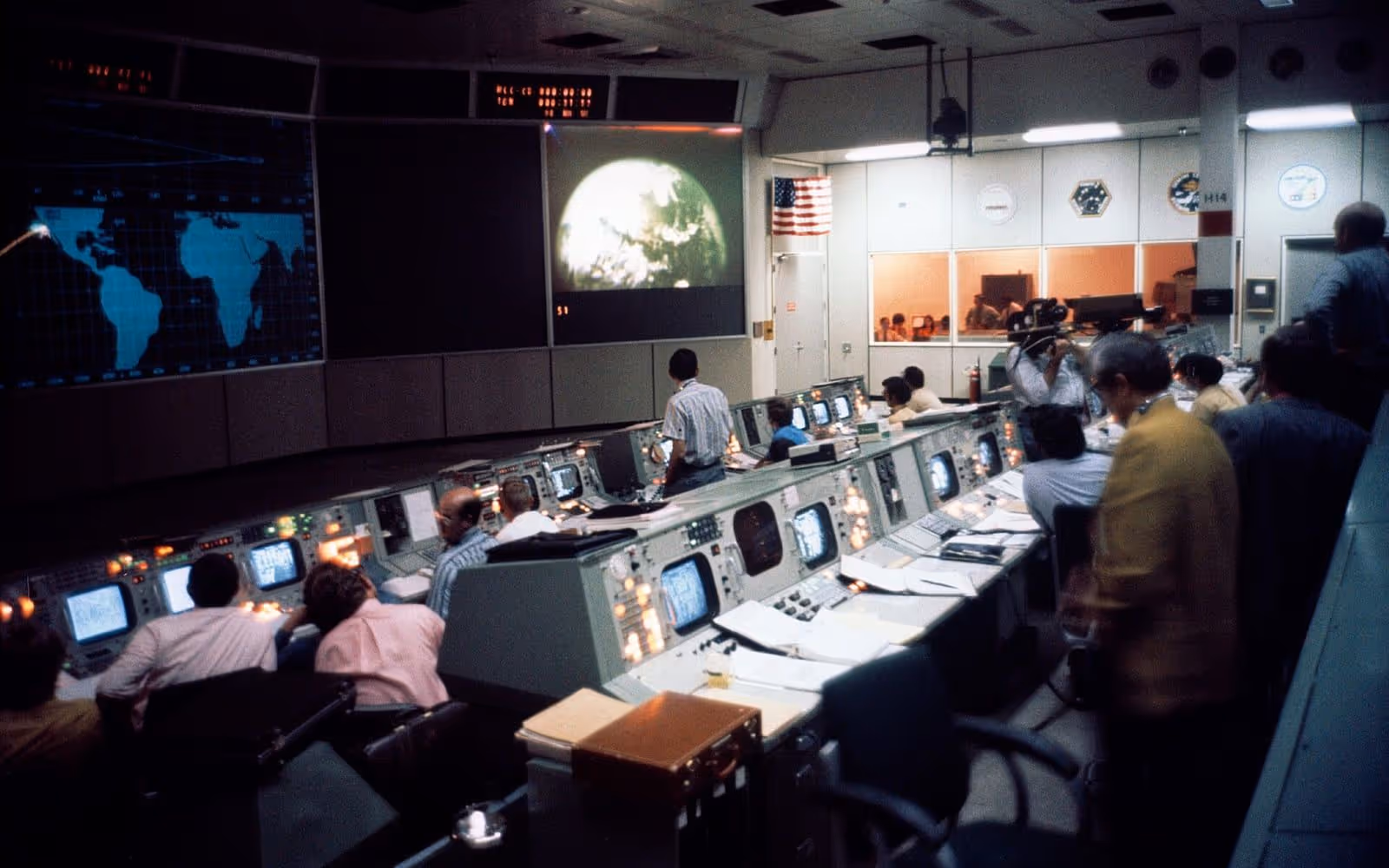 An operations control room with rows of consoles facing a wall of large display screens