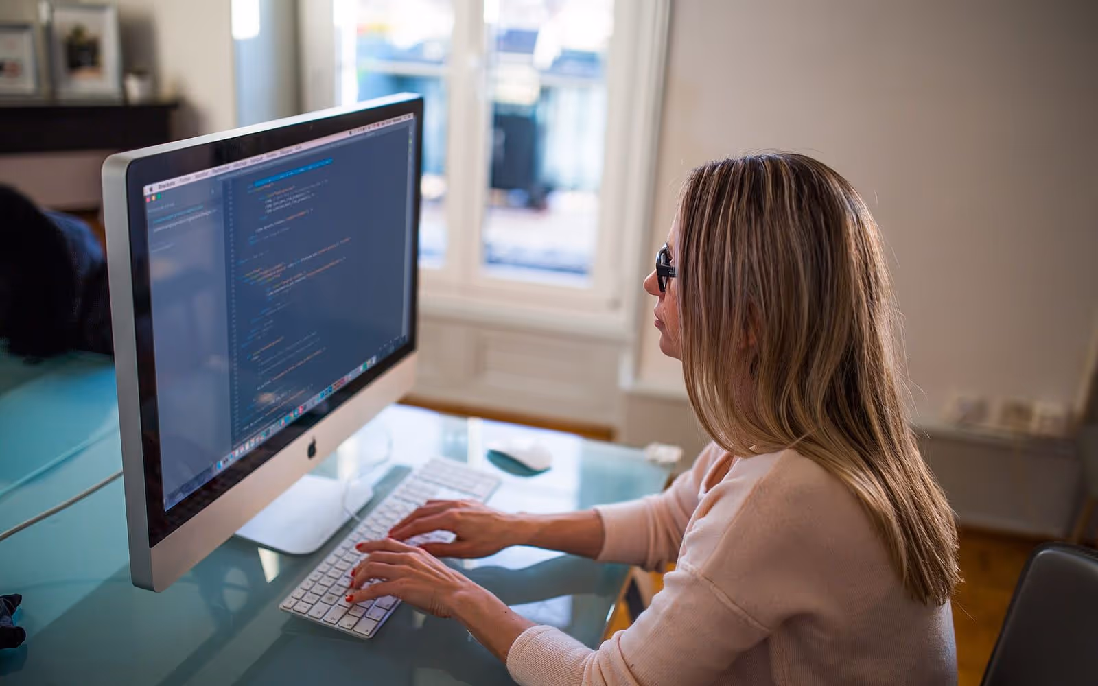 A software developer working at a desk in front of a monitor showing source code