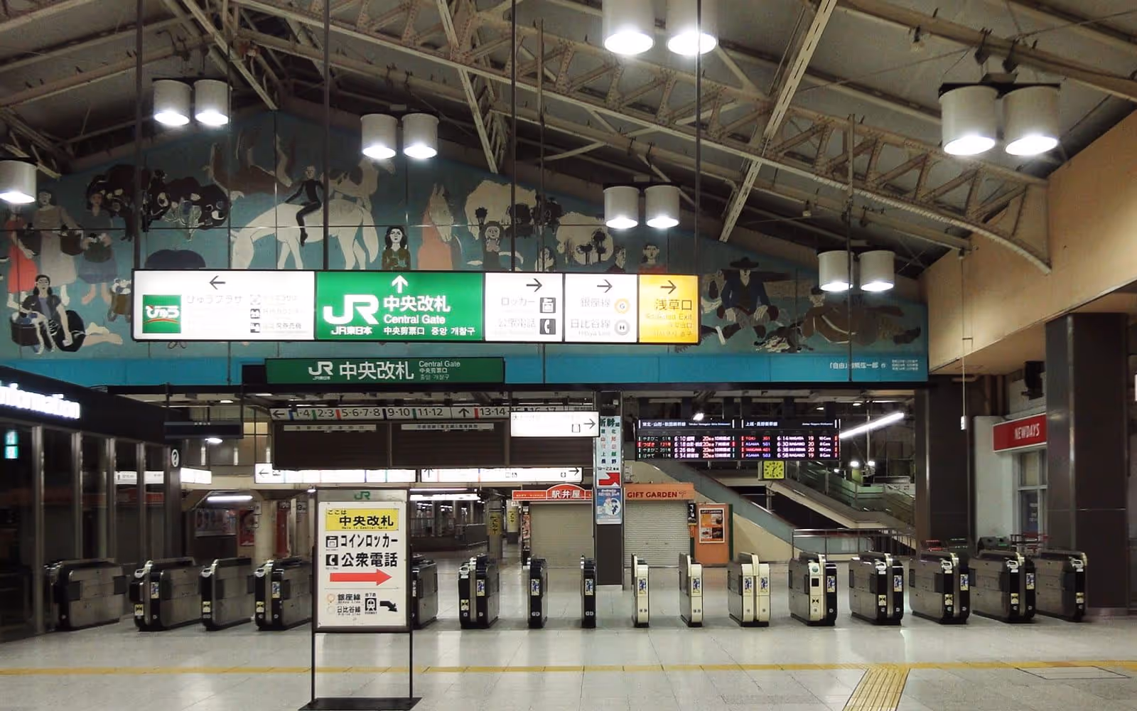 A row of automatic gates inside a station concourse, with people walking through them